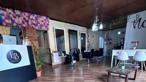 A salon interior with a reception desk, two hairdressing chairs, a wooden table, and a potted plant. - NEIZAN HOTEL (Antigua Guatemala)