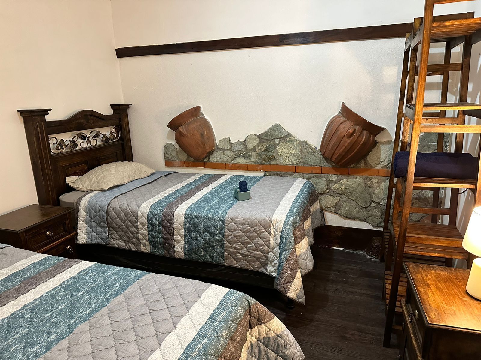 A bedroom with two beds, a wooden headboard, a stone wall, and a wooden ladder.