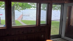 Ein Zimmer mit großen Fenstern mit Blick auf einen See, Holzvertäfelung und einer Stehlampe.