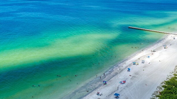 A beach with clear turquoise waters, a sandy shore, and a pier extending into the sea.
