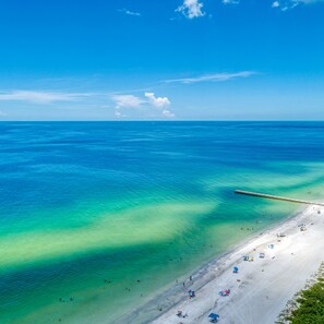 Une plage aux eaux turquoise et limpides, un rivage sablonneux et une jetée qui s’avance dans la mer.