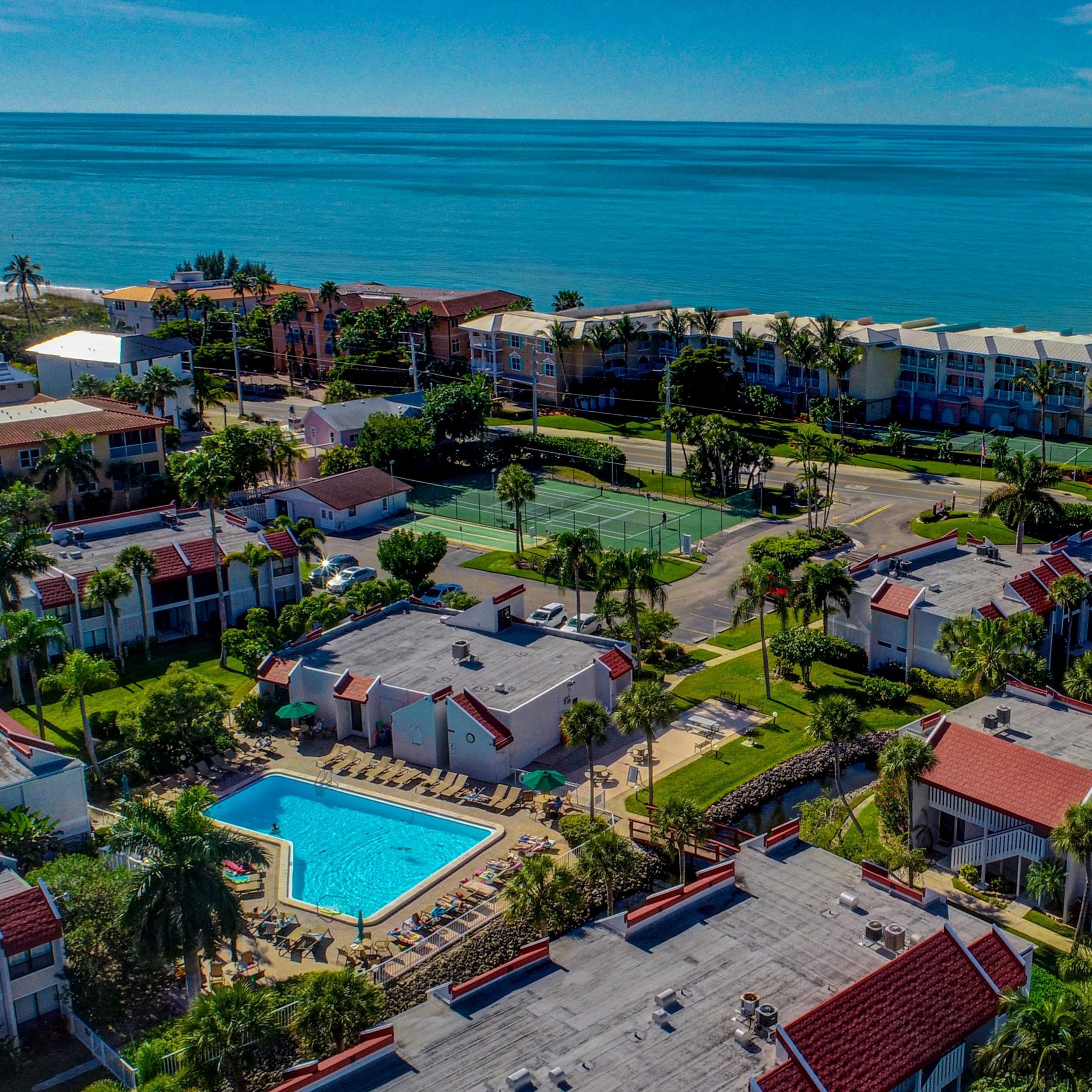 Un complejo turístico con piscina, canchas de tenis y vistas a la playa.