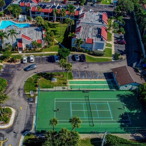 An aerial view of a hotel with multiple buildings, a tennis court, and a parking area.