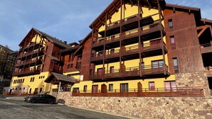 A multi-story building with balconies, a stone facade, and a parked car. - Risoul - Appartement de Standing - 6 Couchages (Risoul)
