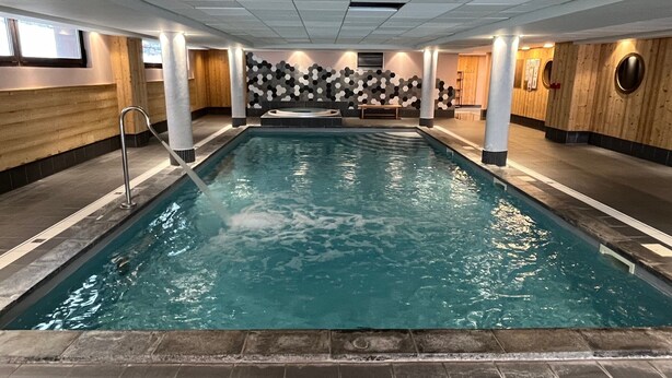 An indoor swimming pool with a tiled floor, wooden walls, and a bench in the center. - Risoul - Appartement de Standing - 6 Couchages (Risoul)