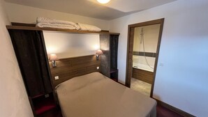 A compact hotel room with a bunk bed, a single bed, bedside lamps, a shower, and a wooden headboard. - Risoul - Appartement de Standing - 6 Couchages (Risoul)