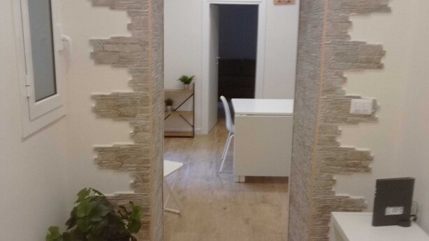 Un pasillo con pared de piedra, una planta en maceta y una mesa blanca con sillas.