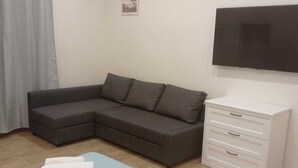 Una sala moderna con un sofá seccional gris, un aparador blanco y un televisor de pantalla plana montado en la pared.