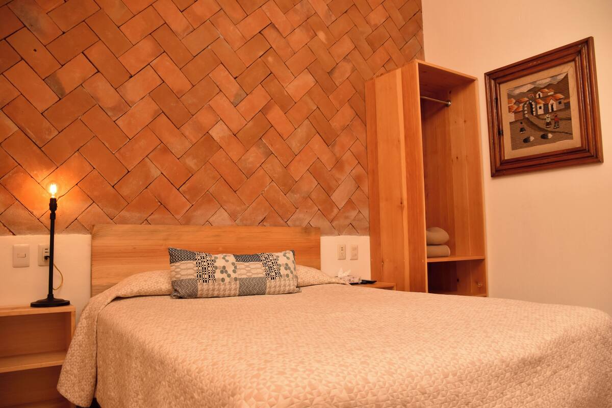 Ein ordentlich bezogenes Bett mit einem gemusterten Kopfkissen, einem Holzkopfteil und einem an der Wand befestigten Bilderrahmen.