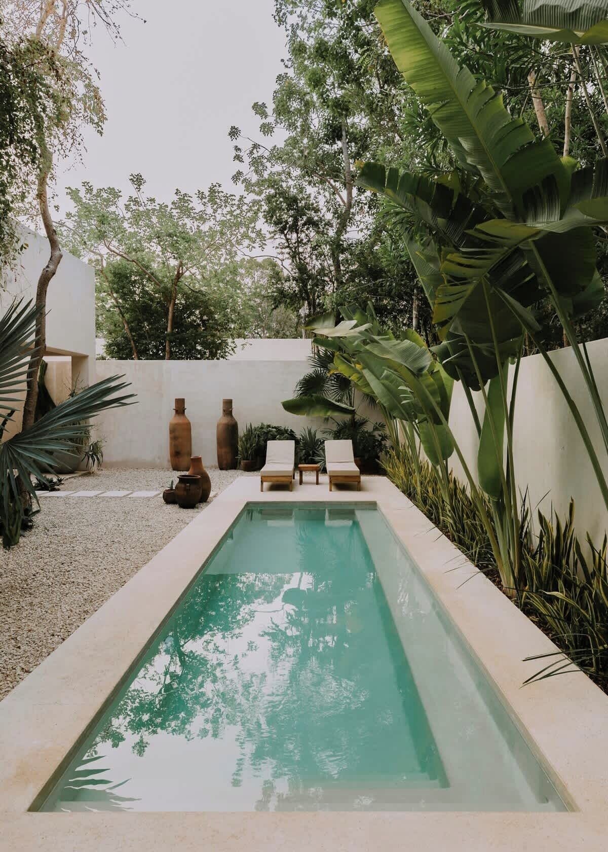 Une piscine rectangulaire agrémentée de deux chaises longues et de deux vases en céramique, le tout installé sur une surface recouverte de gravier.