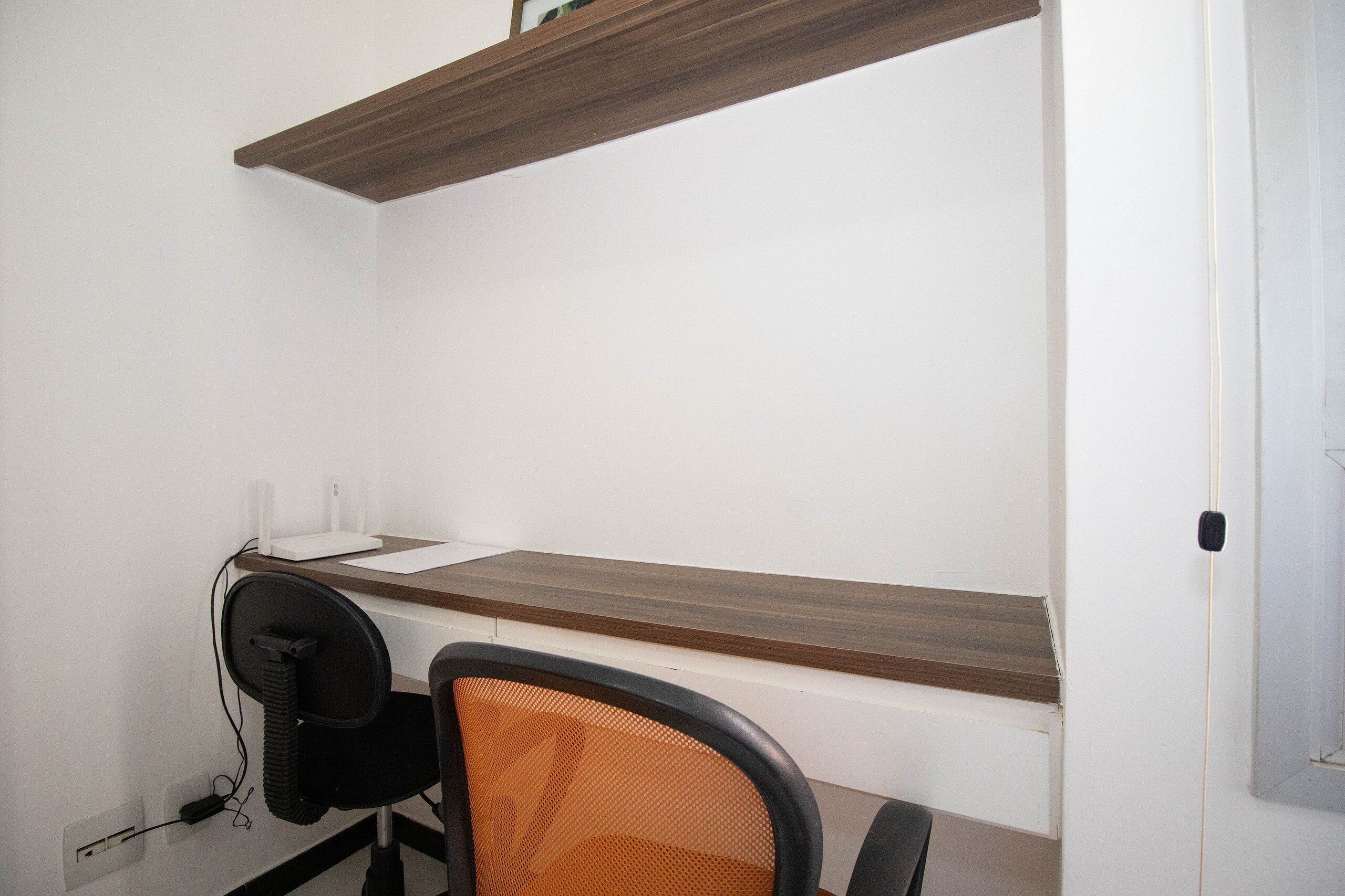 A small office space with a desk, chair, and a shelf above the desk.