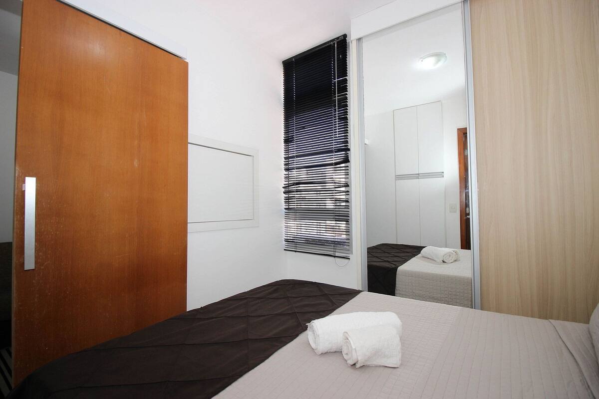 Ein Hotelzimmer mit einem Bett, einem Holzschrank, einem Fenster mit Jalousien und einem Spiegel.