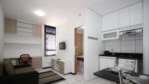 Un espacio habitable compacto con kitchenette, sofá, mesa de comedor y televisor.
