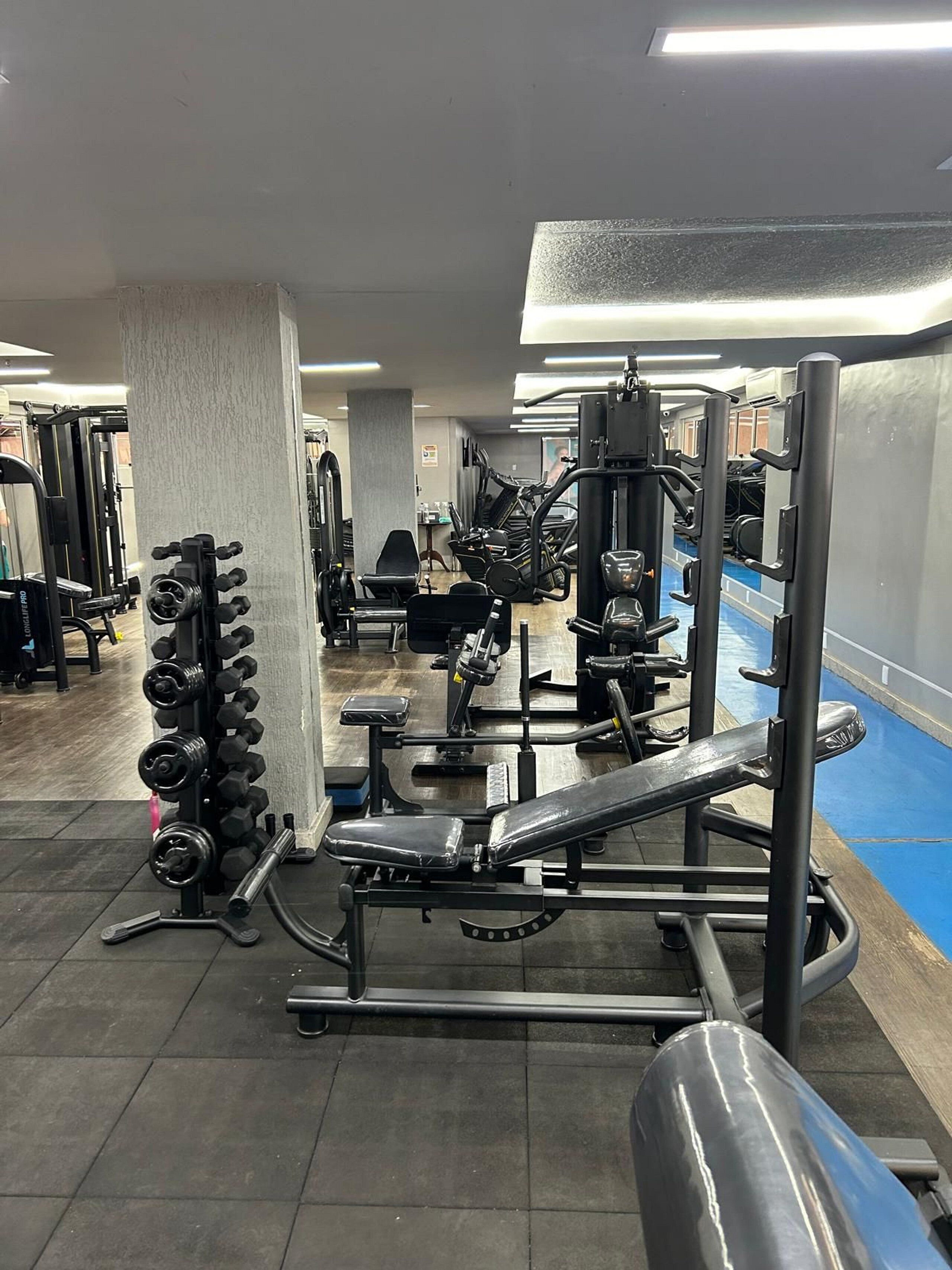 Uma academia com diversos equipamentos de exercícios, incluindo halteres, bancos e aparelhos de musculação.