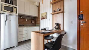 Una cocina compacta con microondas, refrigerador, estantes de madera y un comedor con sillas y una mesa.