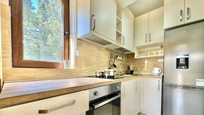 A modern kitchen with a built-in oven, stainless steel refrigerator, and a window with a view of trees. - Central apartments Surina (Budva)