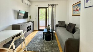 A compact living space with a sofa, a small table, a TV, and a balcony with curtains. - Central apartments Surina (Budva)