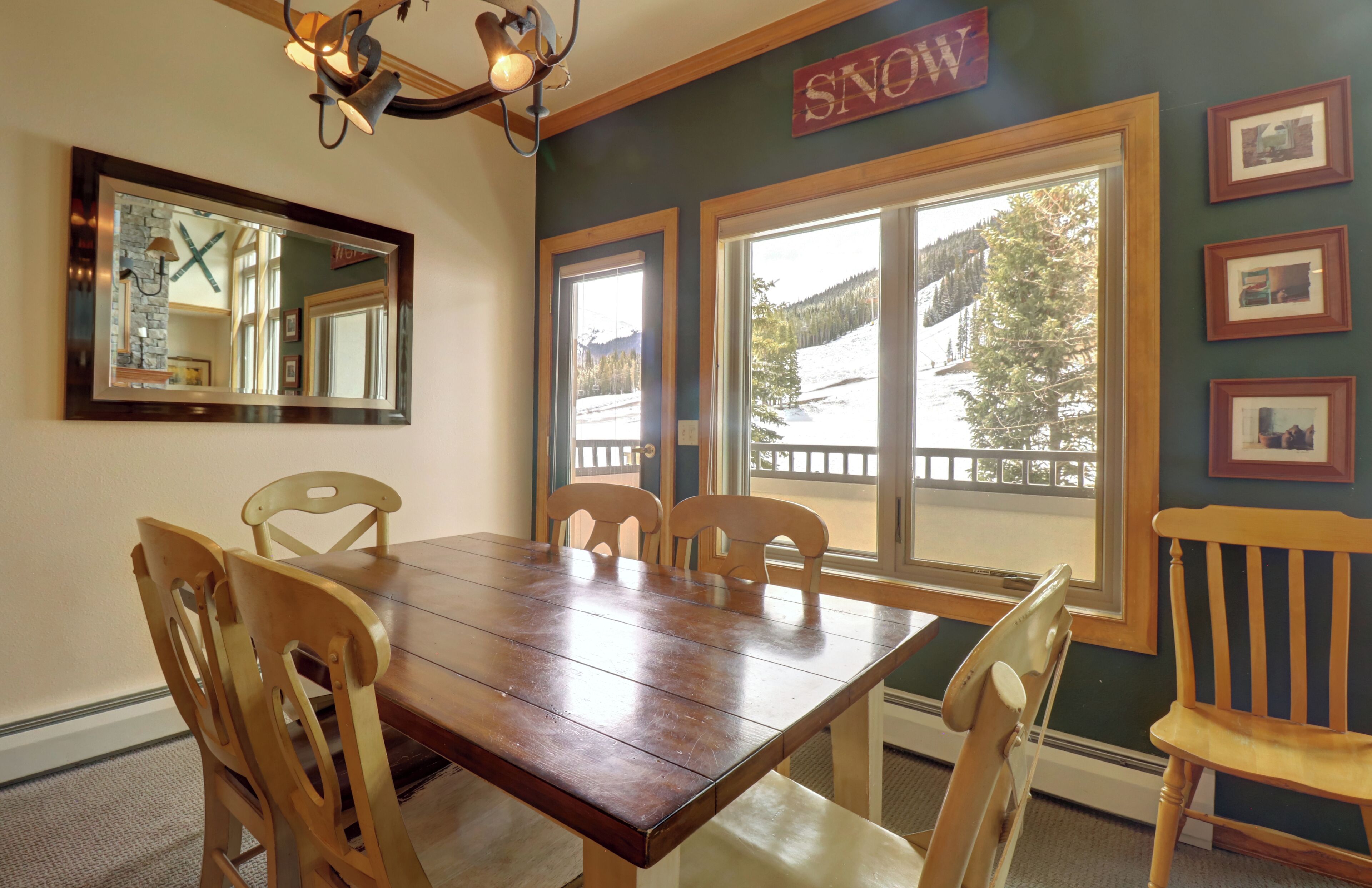 Un comedor con una mesa y sillas de madera, ventanas amplias con vistas a un paisaje nevado, y un cartel que dice 'SNOW'.