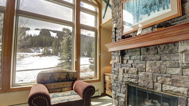 Una habitación acogedora con chimenea de piedra, ventanas amplias con vistas a un paisaje nevado y un sillón mullido.