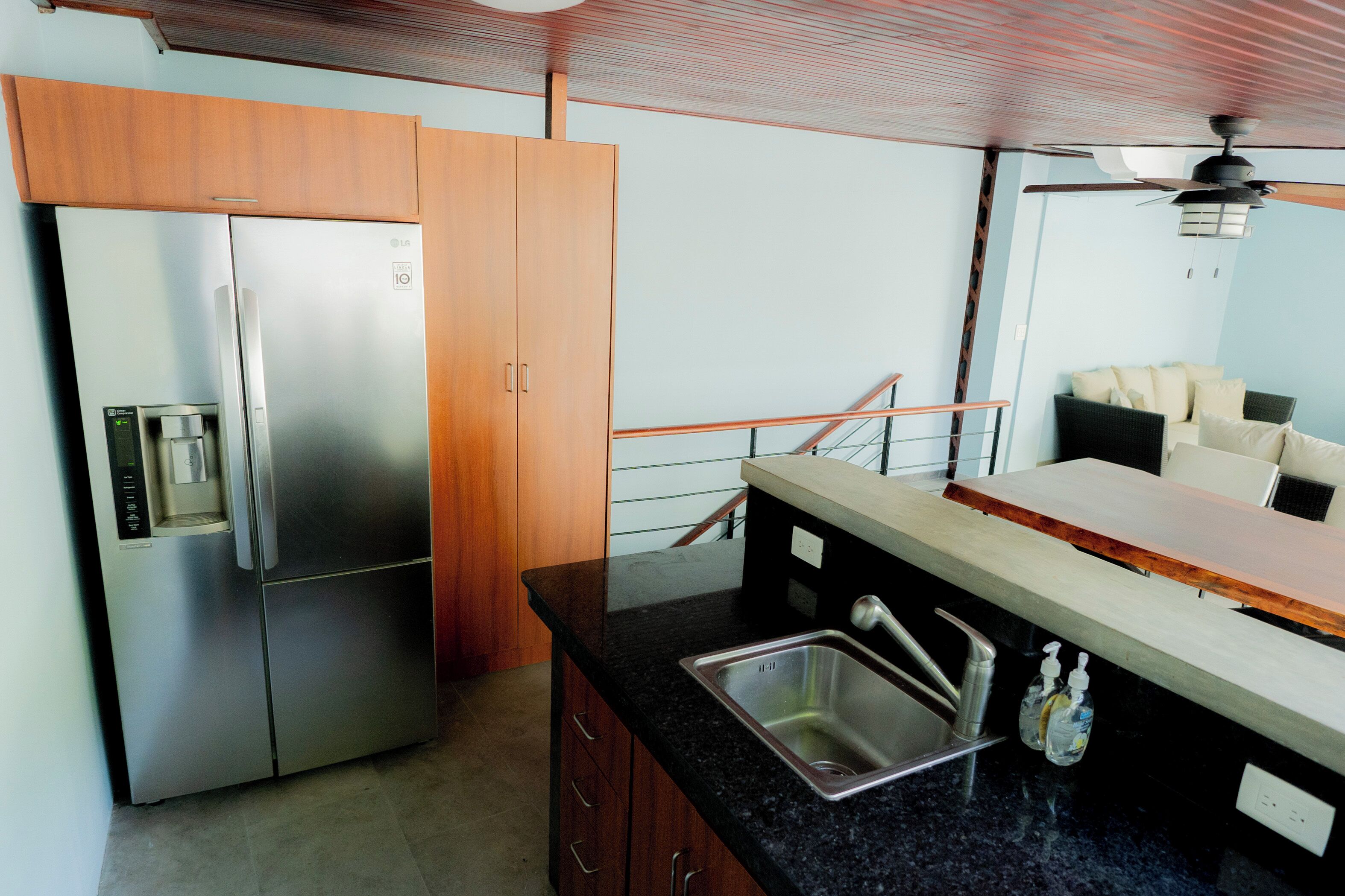 A kitchen with a stainless steel refrigerator, wooden cabinets, a black countertop, a sink, and a ceiling fan.