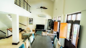 A spacious living area with a high ceiling, a flat-screen TV, a dining table with chairs, and a staircase leading to an upper level. - Una Villa Colonial con Encanto en el Corazón del Casco Antiguo (Panama)