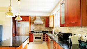 A kitchen with wooden cabinets, stainless steel appliances, a black countertop, and pendant lighting. - Una Villa Colonial con Encanto en el Corazón del Casco Antiguo (Panama)