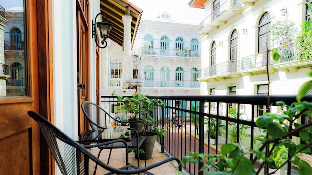 A balcony with a chair, potted plants, and a view of adjacent buildings. - Una Villa Colonial con Encanto en el Corazón del Casco Antiguo (Panama)