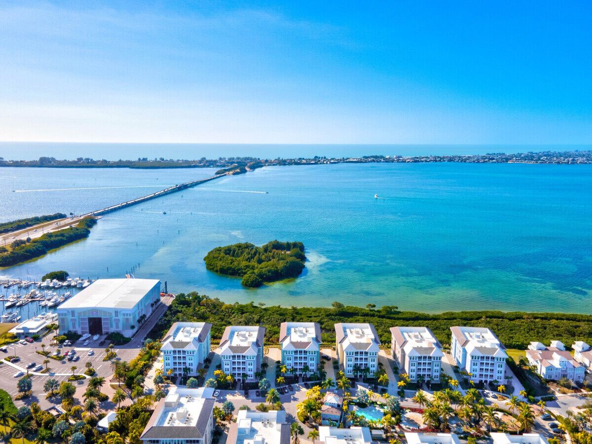 Un hotel frente al mar con varias construcciones blancas, un puerto deportivo y una vista despejada del océano y una pequeña isla.