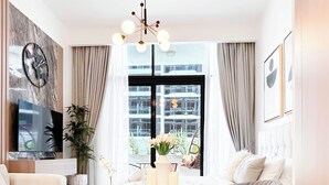 A modern living room with a sofa, a coffee table, a TV, and a large window with curtains. - Elegant Studio With Balcony on the Riviera Dubai (Dubai)