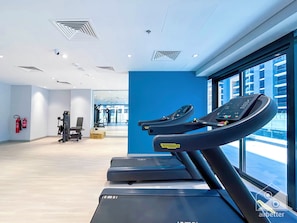 Un gimnasio moderno con cintas de correr, equipo de ejercicio y un amplio ventanal con vistas a la ciudad.