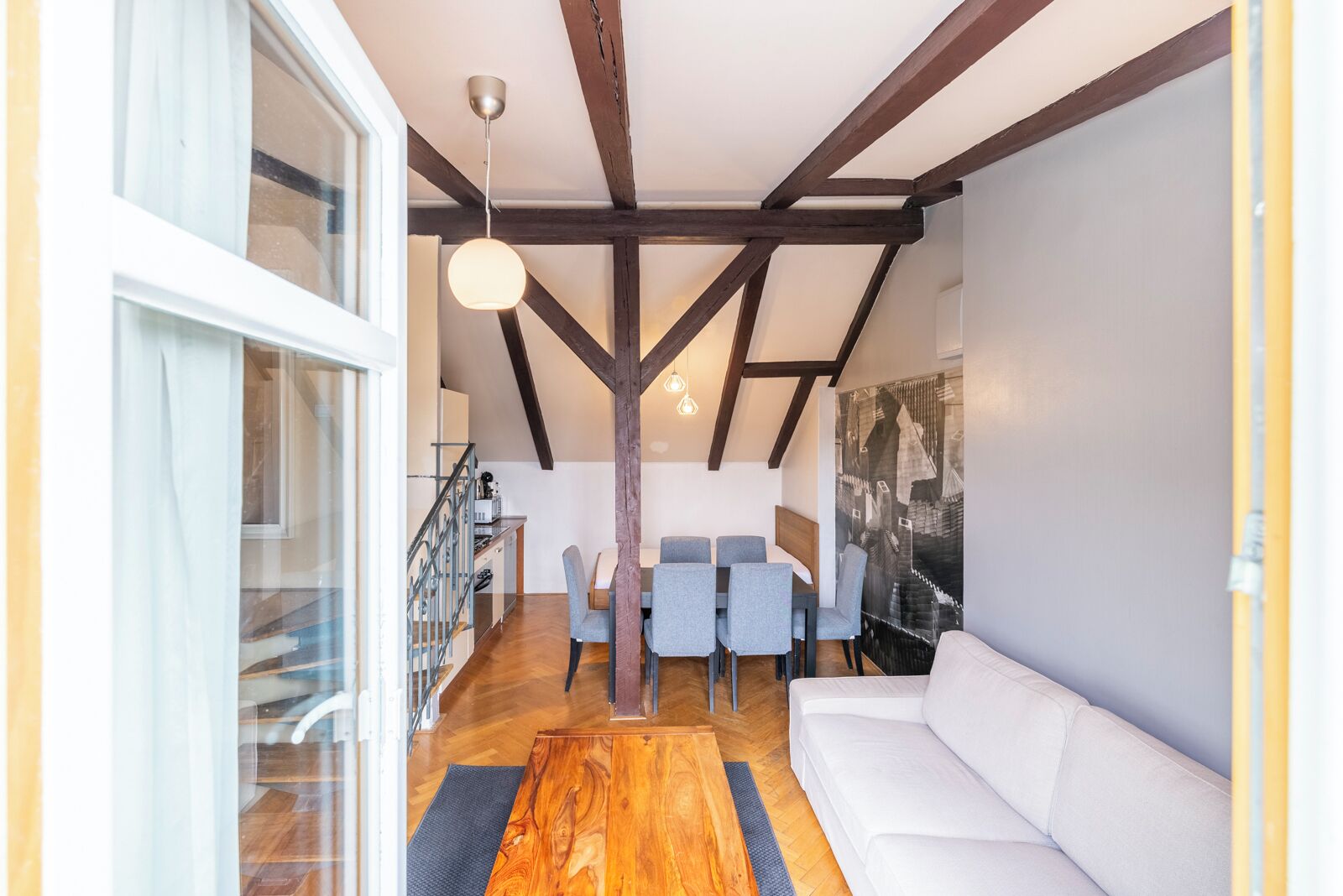 Un interior modern amb zona de menjador, sofà blanc i bigues de fusta.
