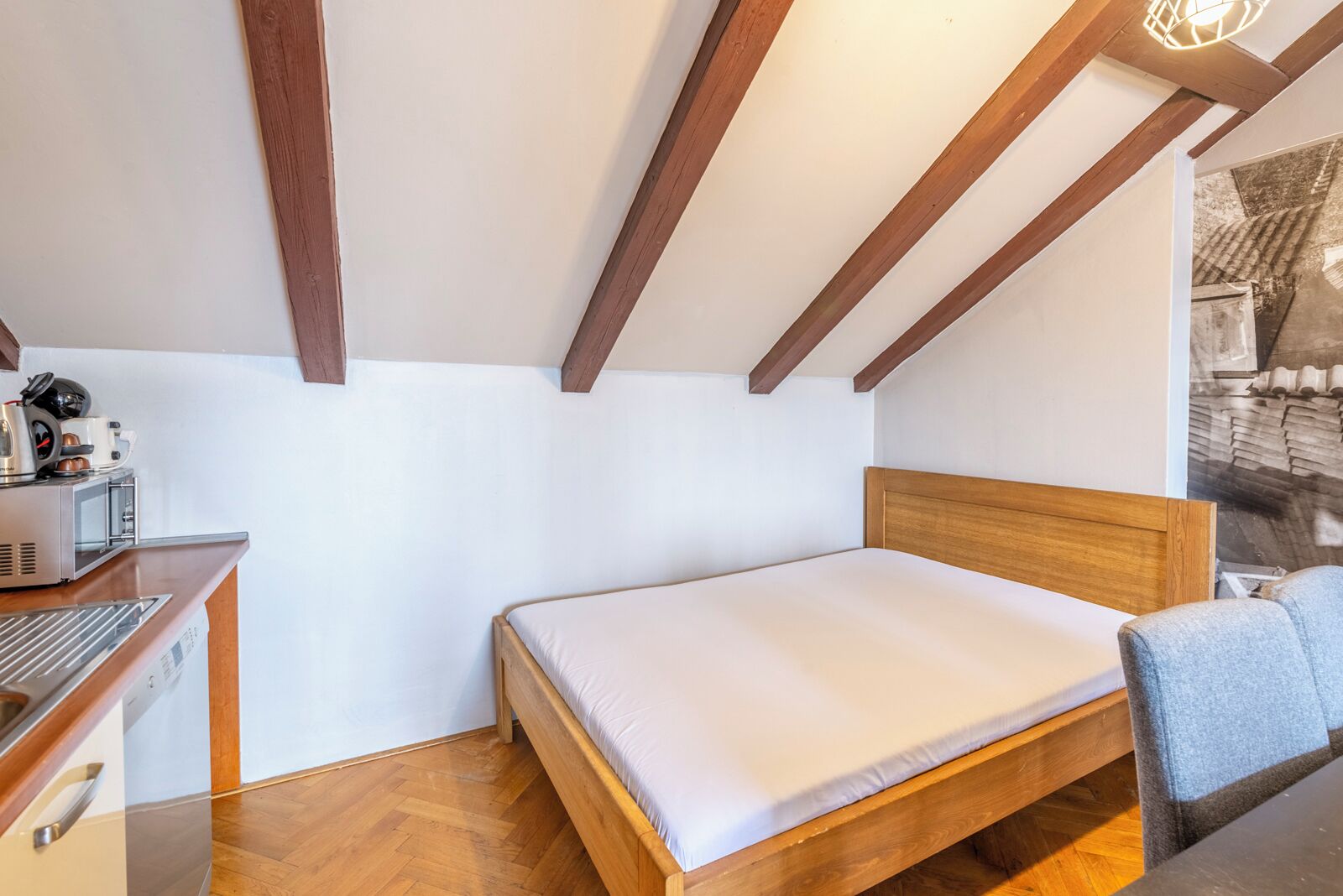 A bedroom with a wooden bed, a small desk with a coffee machine, and a wooden ceiling with exposed beams.