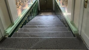 Una imponente escalera con elaboradas esculturas y un piso de baldosas verdes que conduce a una puerta con un panel de vidrio.