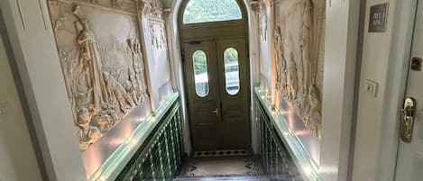 A grand staircase with ornate carvings and a green-tiled floor leading to a door with a glass panel.