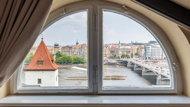 Vista desde una ventana con arco semicircular, que da a un río con un puente y edificios al fondo.