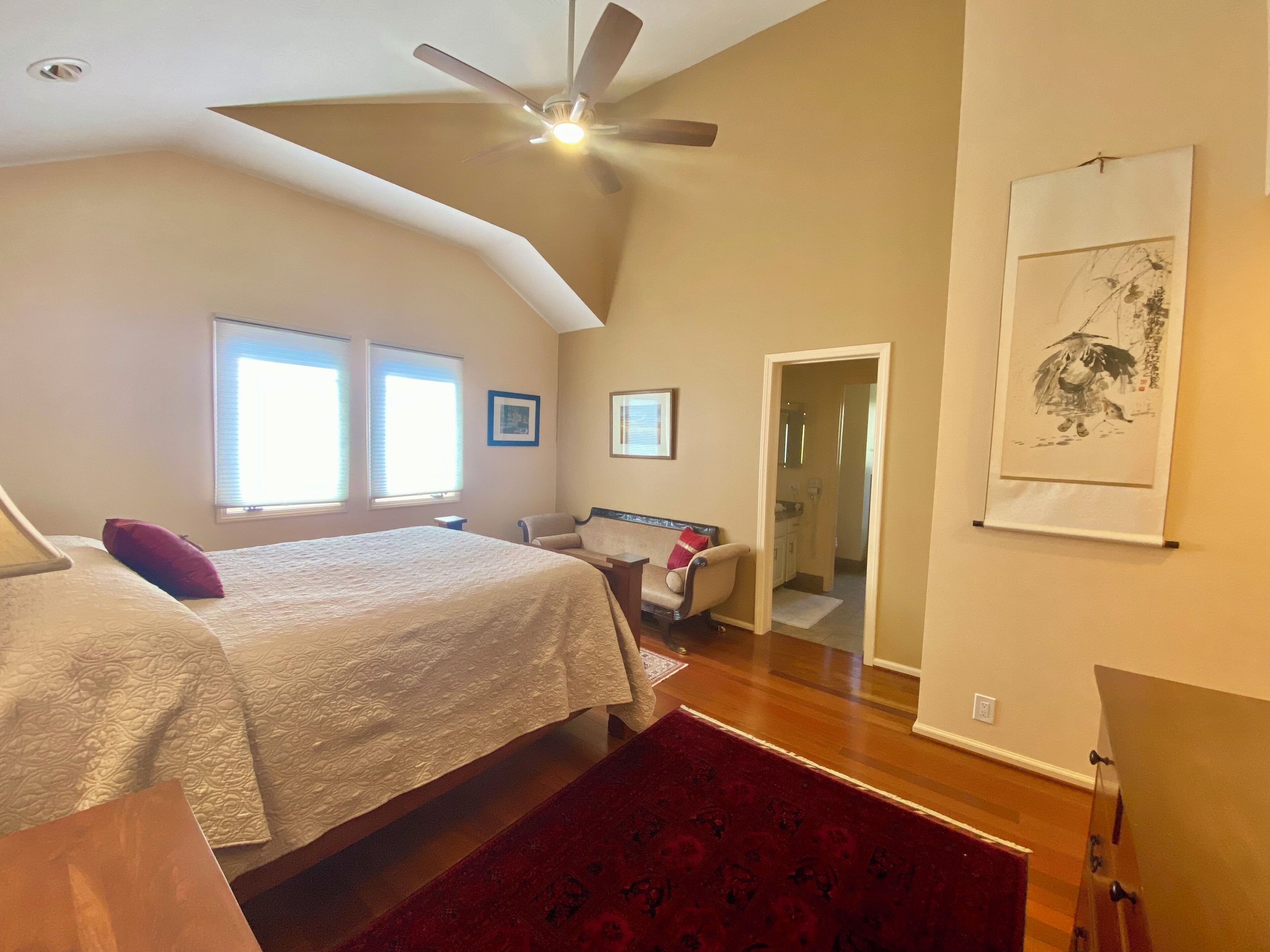 Ein Schlafzimmer mit Bett, Sessel, Deckenventilator und einem Bild an der Wand.