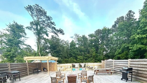 Une terrasse en bois avec une table et des chaises, entourée d’une clôture en bois et d’arbres.