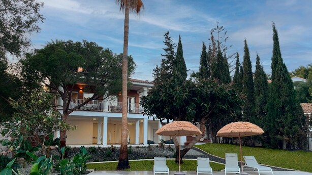 A swimming pool with lounge chairs and umbrellas, surrounded by greenery and a building with a balcony. - Tess Villa Olmos in M Laga (Málaga)