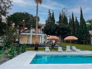 A swimming pool with lounge chairs and umbrellas, surrounded by greenery and a building with a balcony. - Tess Villa Olmos in M Laga (Málaga)