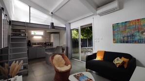 Una cocina moderna con comedor, un sofá negro con cojines naranja y un cuadro abstracto y colorido en la pared.