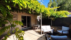 Un patio con una mesa y sillas de comedor, un sofá blanco y una pérgola con plantas trepadoras.
