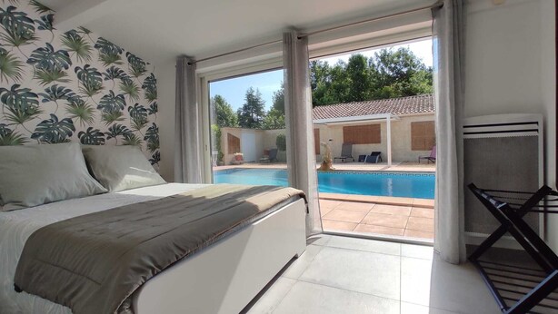 Un dormitorio con una cama grande, vistas a una piscina y una zona exterior cubierta con sillas.