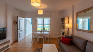 Ett modernt vardagsrum med en matplats, en tv och ett stort fönster med utsikt över stranden.