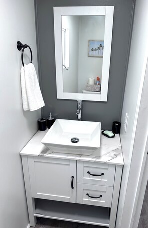 Un baño con un lavabo blanco, un espejo, un perchero y un ventanal con vistas a palmeras.