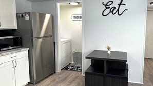 Una cucina moderna con mobili bianchi, un frigorifero in acciaio inossidabile, un forno a microonde e un tavolo in legno scuro con un vaso.