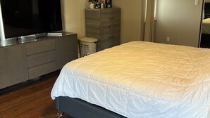 Een slaapkamer met een groot bed, een televisie op een dressoir, een dressoir, een spiegel en een kledingkast.