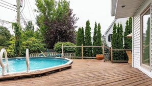 Een houten terras met een hottub, omringd door bomen en een huis.