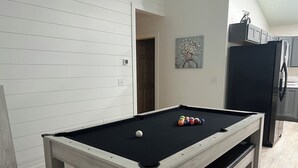 Una mesa de billar con bolas, un refrigerador y un cuadro en la pared.