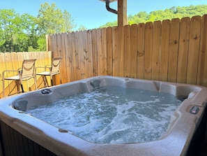 Un bain à remous entouré d’une clôture en bois, avec des chaises en arrière-plan.