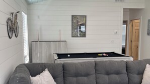 Una sala de estar moderna con un sofá seccional gris, una mesa de billar y una bicicleta colgada en la pared.